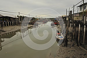 river reflection muddy water moored boat stilt houses cloudy sky