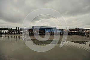 river reflection muddy water moored boat stilt houses cloudy sky