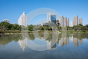 The river reflects the modern city buildings under the blue sky