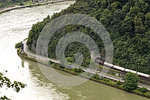 The river Rhine in western Germany flows between the hills covered with forest, visible freight train and traffic lights for ship