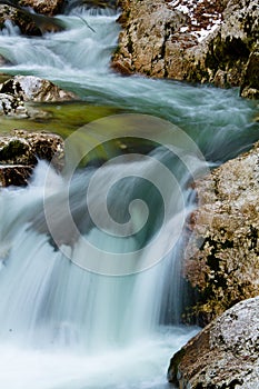 River rocks in smooth satin water flow of waterfall in wintertime