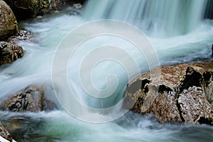 River rocks in smooth satin water flow of waterfall in wintertime