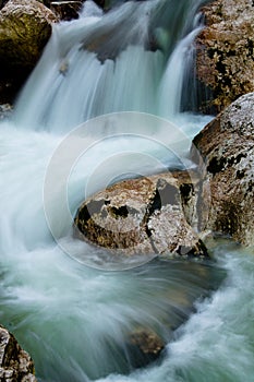 River rocks in smooth satin water flow of waterfall in wintertime