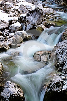 River rocks in smooth satin water flow of waterfall in wintertime