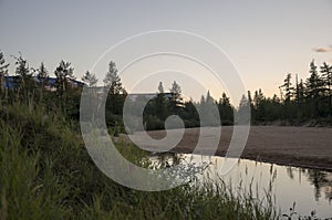 River running across the forest with reflections in the water. Evening  sunset with pink and violets colors in the sky. Silhouette