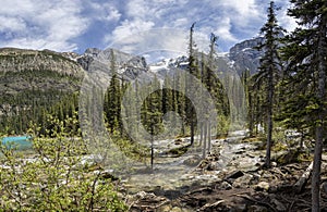 River running though forest into glacial lake Moraine with snow capped mountains in Banff National Park, Alberta, Canada