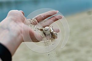 River shells and fine white river sand fall from a woman`s hand