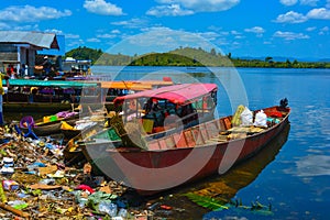 River with simple boats for passenger transportation. Garbage dropped on beach, dirty water