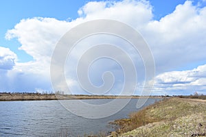 River, sky clouds. Grass fields in the countryside. Meadows and fields form a mosaic