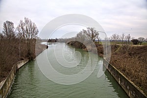 River with the sky and the trees at the edge of it casted in the water in the italian countryside in winter