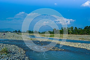 River among stones with trees in background. Blue sky and clouds.