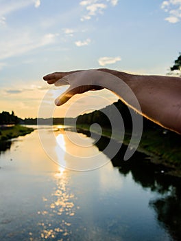 River sun reflection. Catch last sunbeam. Male hand pointing at sun in blue sky at evening time admire landscape