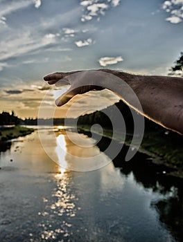 River sun reflection. Catch last sunbeam. Male hand pointing at sun in blue sky at evening time admire landscape