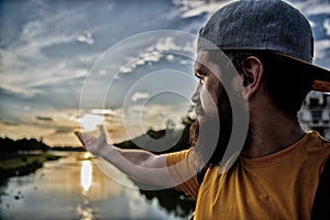 River sun reflection. Man in cap enjoy sunset while stand on bridge. Enjoy pleasant moment. Guy in front of blue sky at