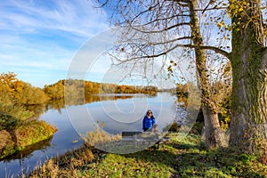 River surrounded by autumn trees against blue sky in background, female hiker standing with her dog