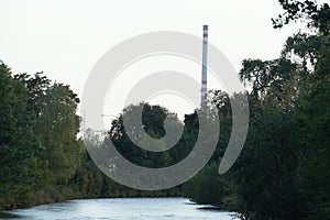 Rieka Turiec v meste Martin na severnom Slovensku s divokou vegetáciou na oboch brehoch. Na obzore je vysoký komín tepla a