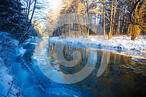 River in winter. Dappled sunlight streaming in mixed forest