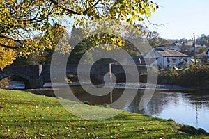 Riverbank, in bright Autumn sunlight, with stone bridge and white hotel.