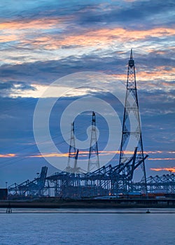 Riverbank with electricity masts and container cranes at twilight