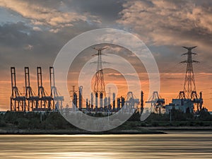 Riverbank with silhouettes of container terminal cranes during a sunset, Port of Antwerp, Belgium