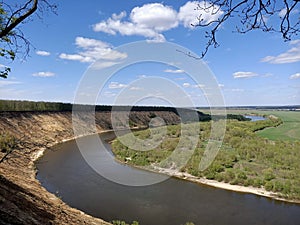 Riverbend in deep spring forest with green trees on the bank of the river and sands under blue sky