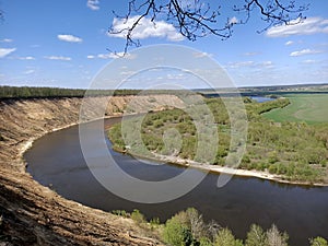 Riverbend in deep spring forestm with green trees on the bank of the river and sands under blue sky