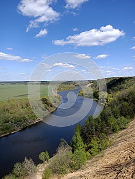 Riverbend in deep spring forestm with green trees on the bank of the river and sands under blue sky