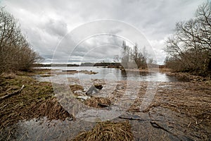 riverside landscape in latvia with dark water and dirty shore line