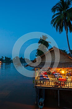 Riverside restaurant near Mekong River at twilight. Coconut trees silhouette, Beautiful lighting, restaurant and sunset sky