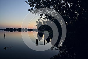 Riverside at sunset with its reflection casted in the water at sunset seen from afar