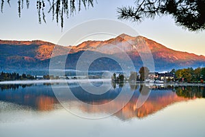 The riverside village and mountains reflect the water in the misty morning at Lake Wolfgang