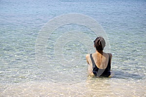 Beautiful young woman in a black swimsuit sits on the sand of a beach in Makarska, Croatia.