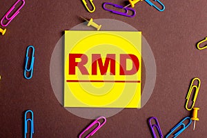 RMD is written in red on a yellow sticker on a brown background next to multi-colored paper clips photo