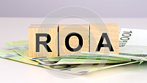 ROA - acronym Return On Assets. text on wood cubes with euro bills