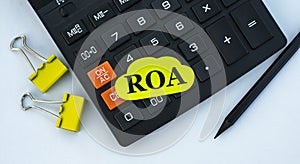 ROA - word on yellow note sheet on white background with calculator, pencil, green sheet and paper clips