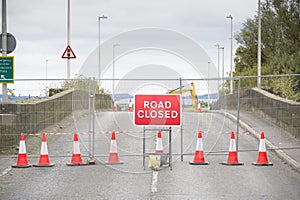 Road ahead closed sign with traffic cones and red barrier fence crossing