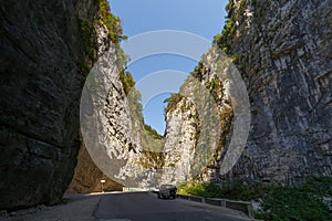 Road along the bottom of a deep canyon. An off-road car is parked at the side of the road