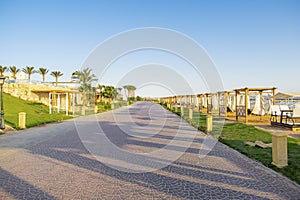 Road along lots of wooden furniture for rest, deck chair bed, gazebo on sand beach with curtains, tropical sea luxury resort.