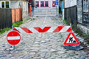 Road barrier with warning and prohibition road signs on an old paved street