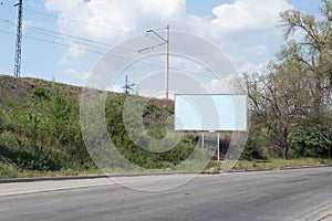 Road billboard, against the background of green trees of the road, an empty ad-free billboard along the road