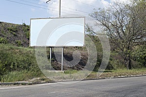 Road billboard, against the background of green trees of the road, an empty ad-free billboard along the road. Advertising,