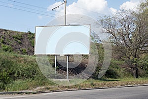 Road billboard, against the background of green trees of the road, an empty ad-free billboard along the road. Advertising,