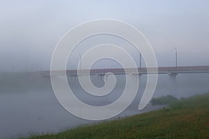 Road bridge over the river covered with predawn mist