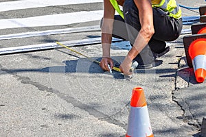 A road builder on the asphalt makes the markings of a pedestrian crossing on a summer day