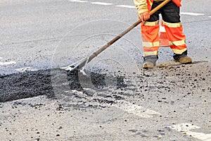 A road builder collects fresh asphalt on part of the road and levels it for repair in road construction.