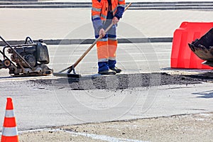 The road builder evenly distributes part of the asphalt with a wooden level on a part of the road fenced with an orange cone and a