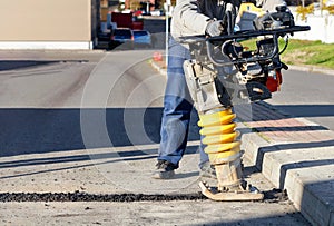 A road builder uses a vibration rammer to repair an asphalt road section