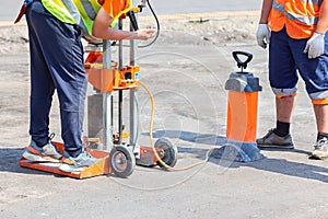 Road builders set up a gasoline drilling machine to cut asphalt concrete samples on a sunny day
