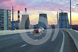road with cars passing in succession with heat power plant at sunset in big city