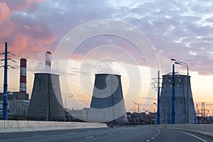 road with cars passing in succession with heat power plant at sunset in big city